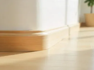 Close-up of a curved wall meeting the floor with smooth, neatly installed wooden quarter round trim in a bright, modern home interior.