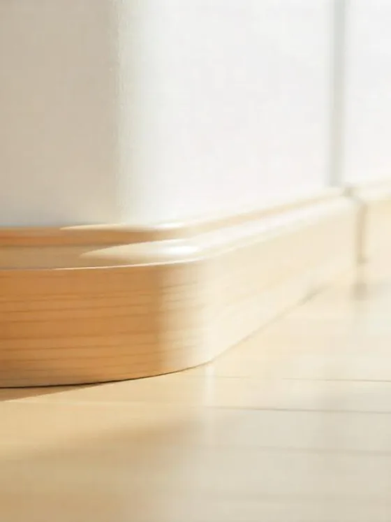 Close-up of a curved wall meeting the floor with smooth, neatly installed wooden quarter round trim in a bright, modern home interior.